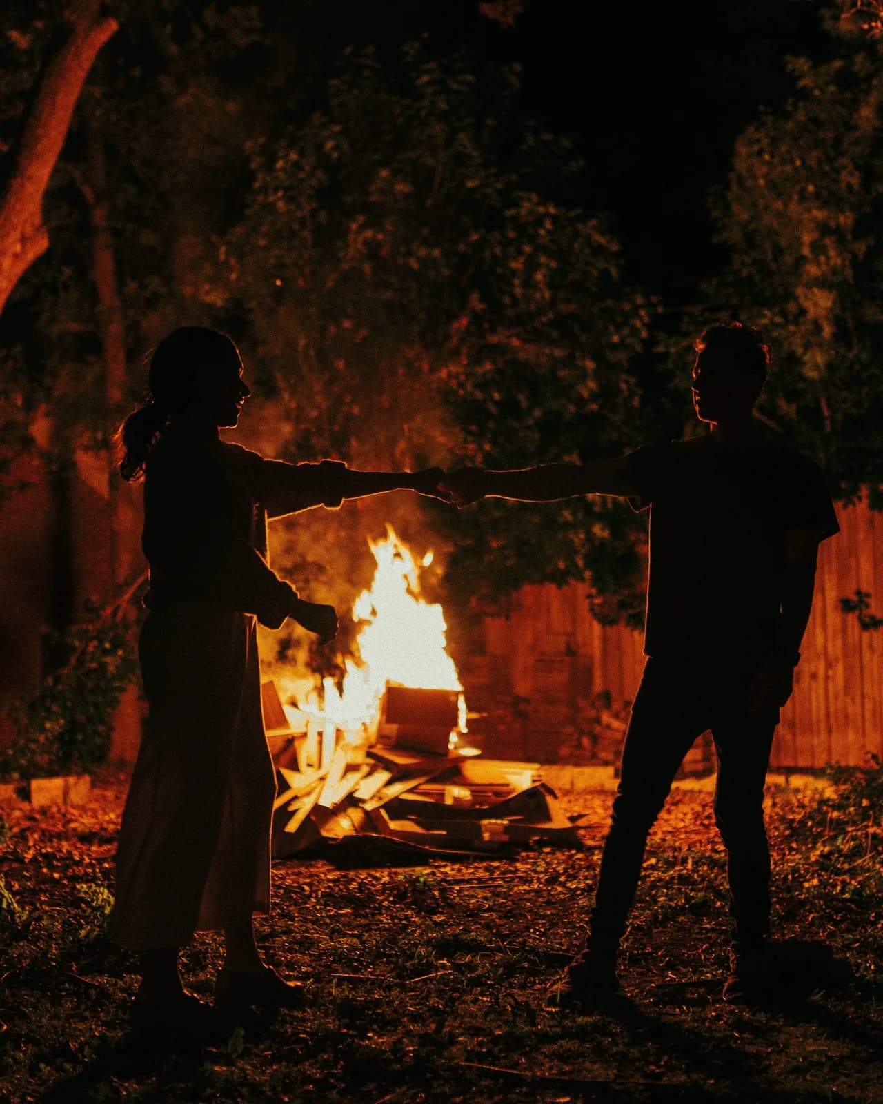 A couple together by a backyard fire at night